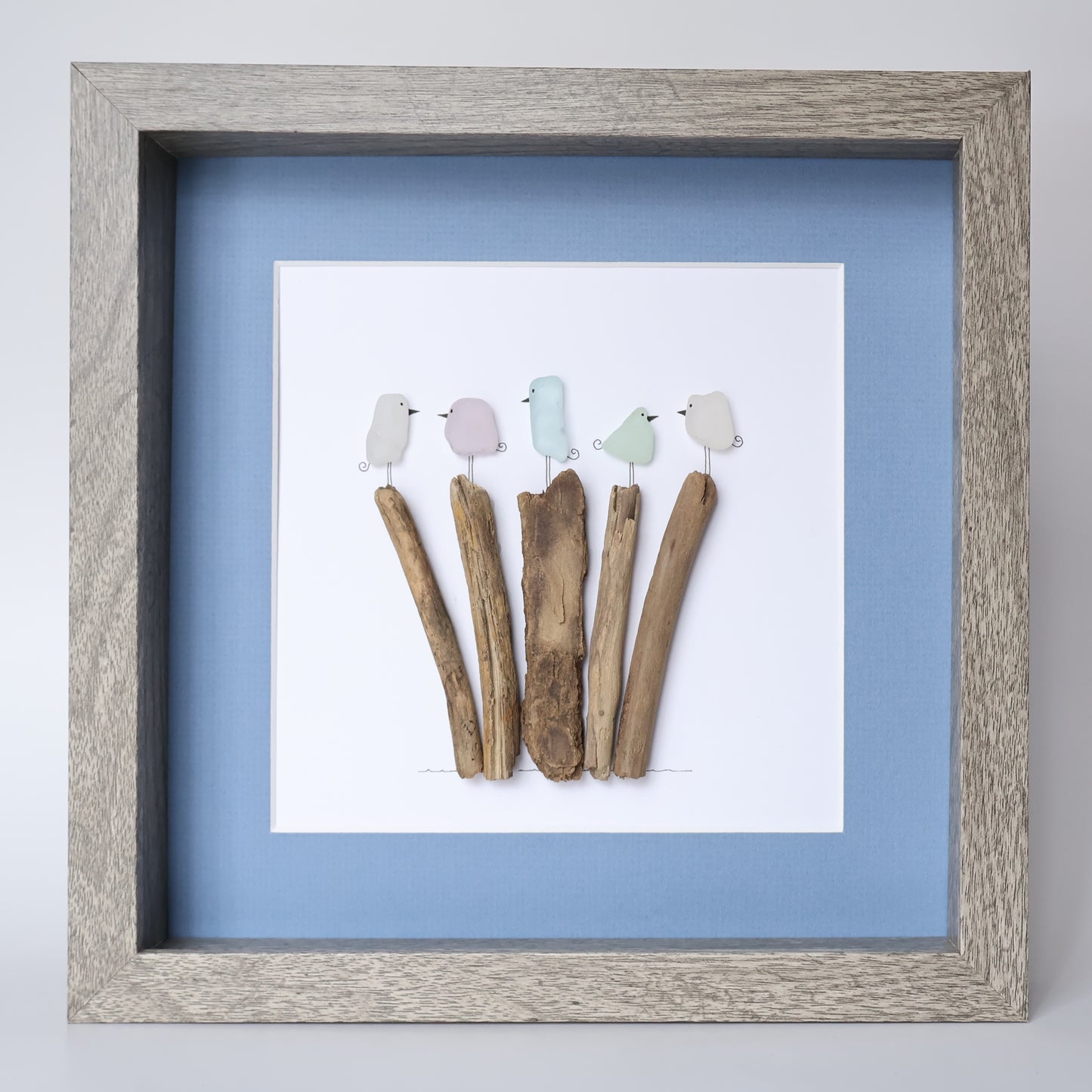 Framed artwork with colorful birds on sticks against a light blue background