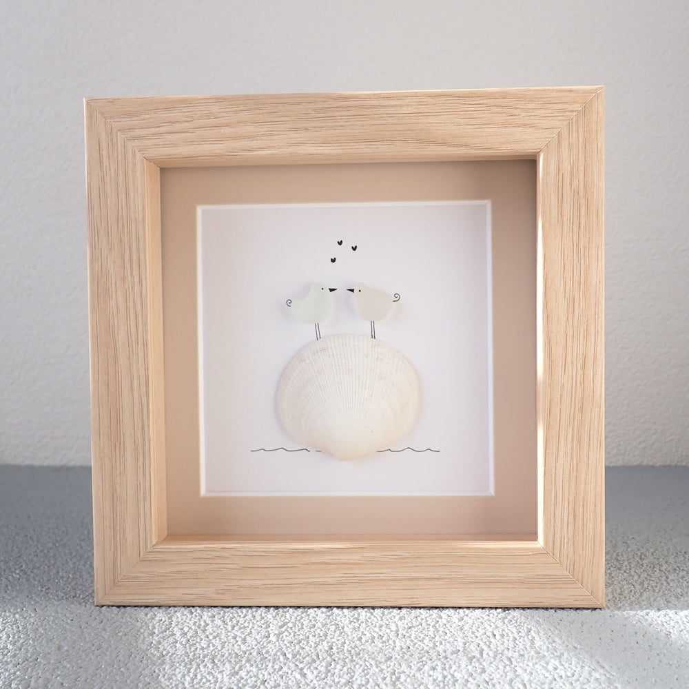 framed picture of two sea glass birds in love standing on a white shells